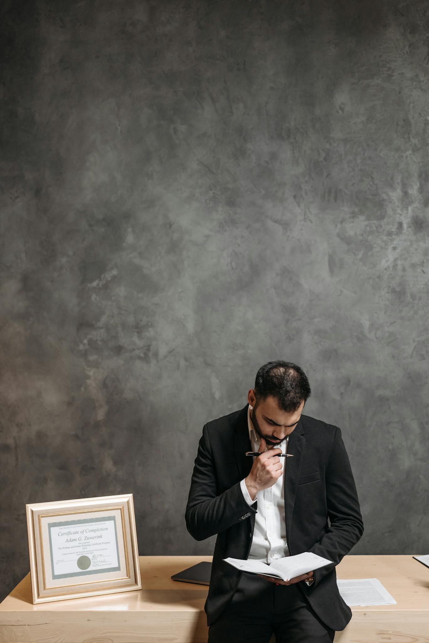 A professional man in a suit reading paperwork thoughtfully in an office.