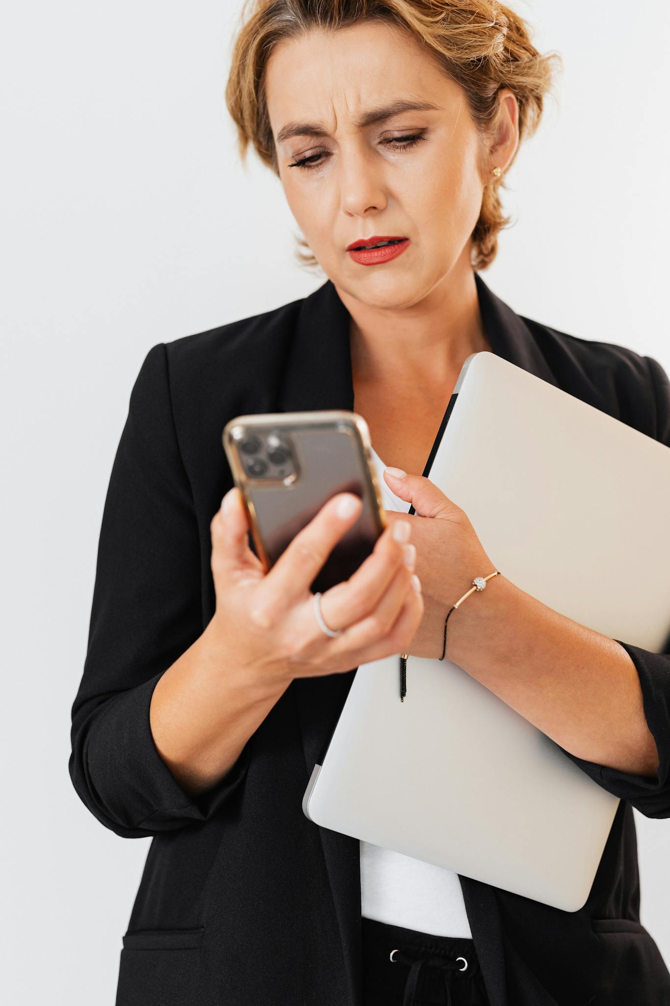 Confident businesswoman multitasking with smartphone and laptop indoors.